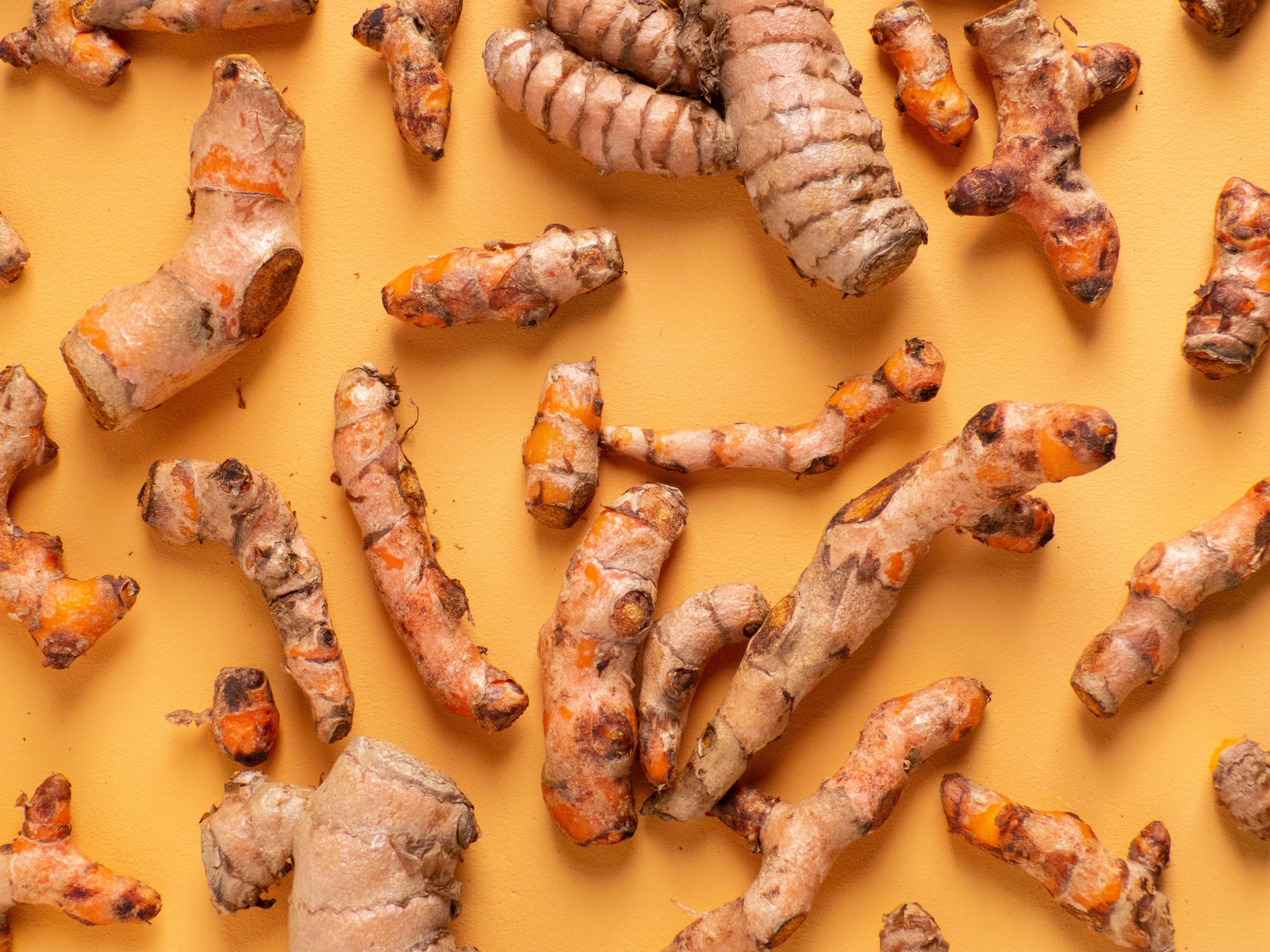 A photo of raw turmeric root used for inflammation and muscle soreness on a yellow background
